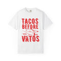 A cartoon character shaped like a taco, with the phrase “Tacos Before Vatos” printed in a bold, colorful retro 1970s font on a vintage white Comfort Colors T-shirt.