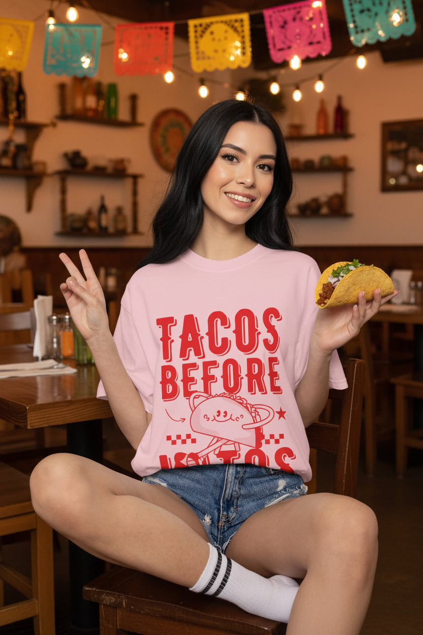 A cartoon character shaped like a taco, with the phrase “Tacos Before Vatos” printed in a bold, colorful retro 1970s font on a vintage Comfort Colors T-shirt.